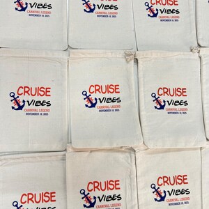 May include: A collection of off-white cotton drawstring pouches, each featuring a printed design with a blue anchor, a red ship's wheel, and the text CRUISE VIBES, CARNIVAL LEGEND, NOVEMBER 10, 2025, arranged in a grid pattern on a flat surface.