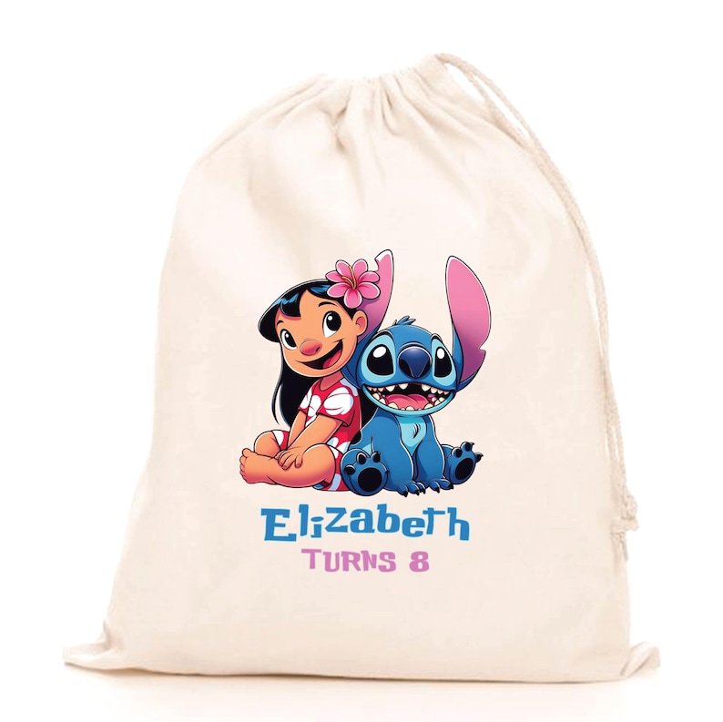 May include: A cream-coloured drawstring bag featuring a colourful graphic of Lilo and Stitch. Below the characters, the text reads "Elizabeth" in blue letters and "Turns 8" in pink letters. The bag is made of a light-coloured fabric with a drawstring closure.