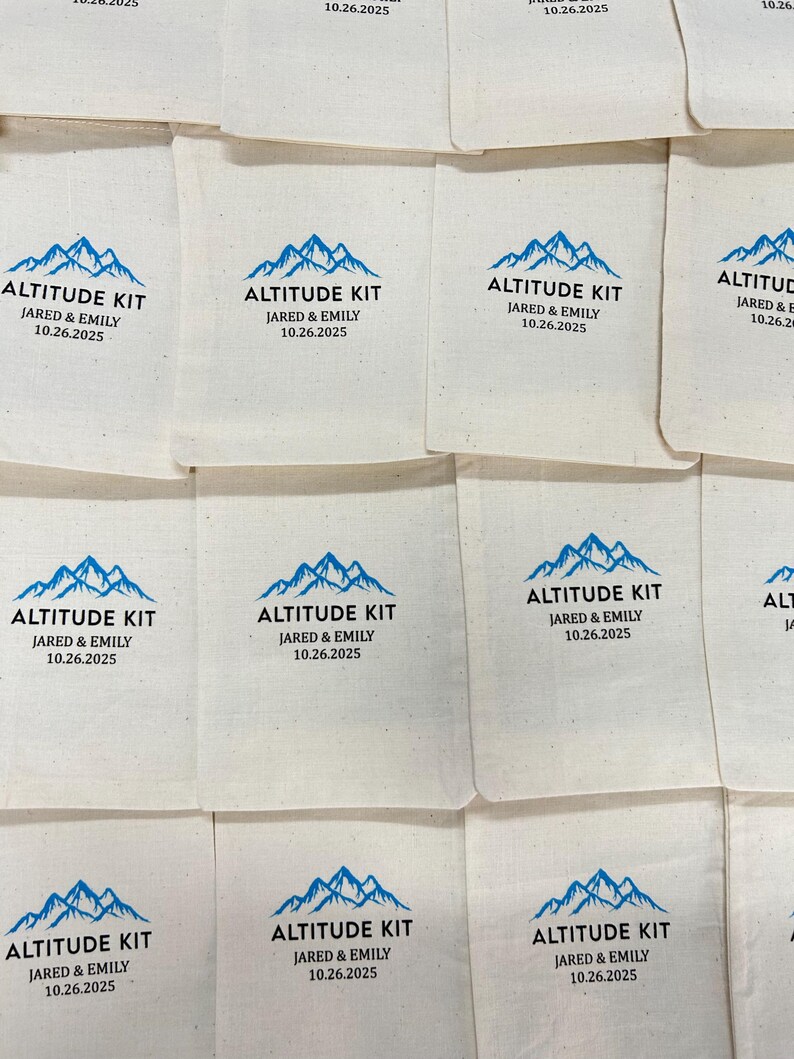 May include: A collection of off-white fabric drawstring pouches featuring a blue mountain graphic and black text that reads ALTITUDE KIT, JARED & EMILY, and the date 10.26.2025. The pouches are arranged in a grid pattern, showing the same design.