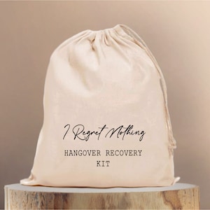 Könnte beinhalten: Eine weiße Kordeltasche mit dem Aufdruck "I Regret Nothing" und "Hangover Recovery Kit".
