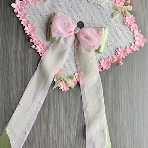 May include: A graduation cap decorated with pink paper flowers and a pink bow with a rhinestone center. The cap has a white background with musical notes and the text "I made it out". Ribbons with pink beads hang from the cap.