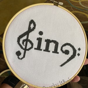 May include: A white embroidery hoop with a black musical note and the text "Sing: 9" embroidered on it.