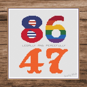 May include: Cross-stitch artwork displaying the numbers 86, with the 6 in rainbow colours, and 47 in orange. The text "LEGALLY AND PEACEFULLY" is below. The piece is framed on a white background.