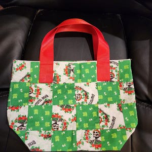 May include: A small tote bag with a green and white patchwork design featuring a floral and skeleton print. The bag has red handles and the words "Grateful Dead" are visible on the fabric.