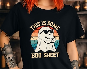May include: Black t-shirt with a retro design featuring a ghost wearing sunglasses and the text "THIS IS SOME BOO SHEET." The design has a vintage sunset color scheme. The shirt is a Halloween-themed apparel.