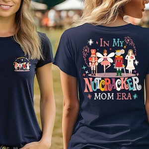 May include: Navy blue t-shirt with a colorful graphic of Nutcracker characters and the text "In My Nutcracker Mom Era" on the back. A smaller version of the graphic is on the front pocket area.