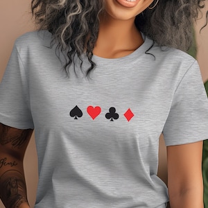 Op de afbeelding: Een lichtgrijs t-shirt met de vier speelkaartsymbolen: schoppen, harten, klaveren en ruiten. De symbolen zijn in zwart en rood en horizontaal over de borst geplaatst.