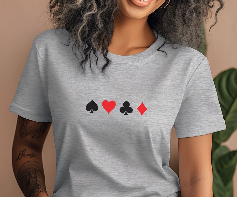 Op de afbeelding: Een lichtgrijs t-shirt met de vier speelkaartsymbolen: schoppen, harten, klaveren en ruiten. De symbolen zijn in zwart en rood en horizontaal over de borst geplaatst.