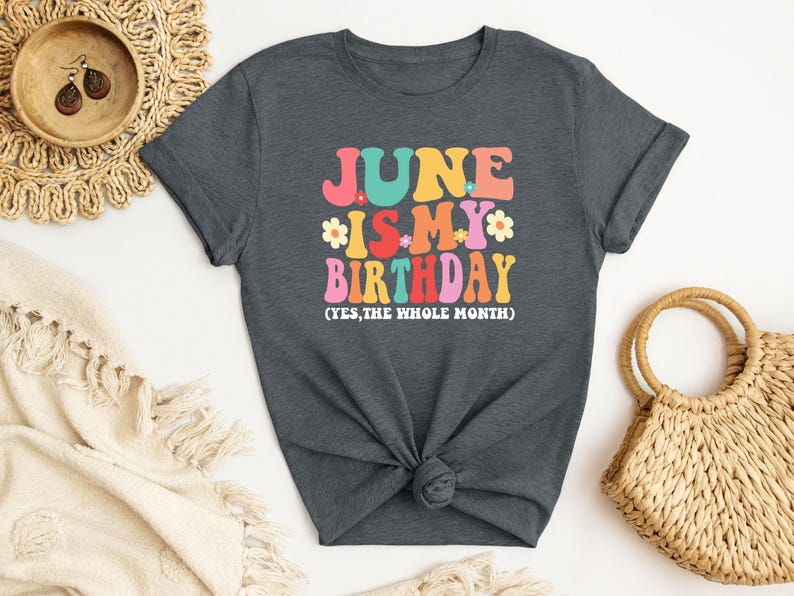 May include: A dark gray t-shirt with the text "June is my birthday (yes, the whole month)" in colorful retro lettering with flowers.