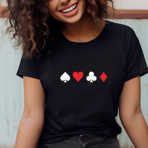 Op de afbeelding: Zwart t-shirt met witte en rode speelkaartsymbolen: schoppen, harten, klaveren en ruiten. De symbolen zijn horizontaal uitgelijnd. Het shirt is gemaakt van een zacht materiaal.