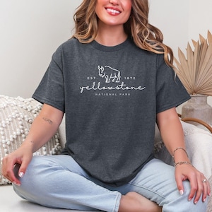 May include: Dark grey t-shirt with the text "Yellowstone National Park" and a bison graphic. The shirt includes the text "Est. 1872". The t-shirt is a comfortable, casual style.
