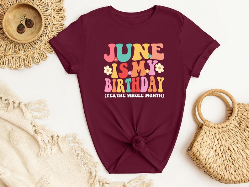 May include: A maroon t-shirt with the text "June is my birthday (yes, the whole month)" in colorful retro lettering.