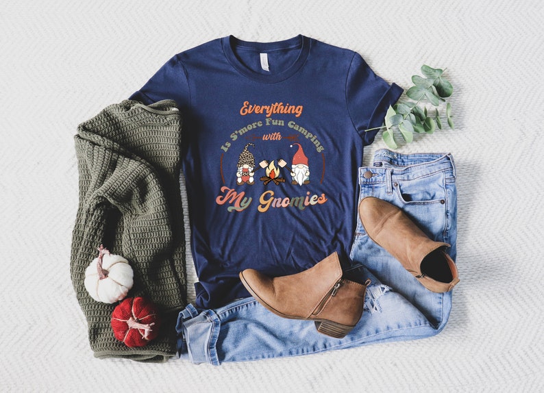 May include: A navy blue t-shirt with a graphic of three gnomes around a campfire. The text on the shirt reads "Everything is S'more Fun Camping with My Gnomies".