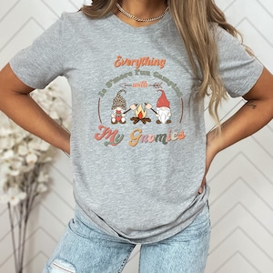 May include: A gray t-shirt with a graphic of three gnomes roasting marshmallows around a campfire. The text on the shirt reads "Everything is S'more Fun Camping with My Gnomies".