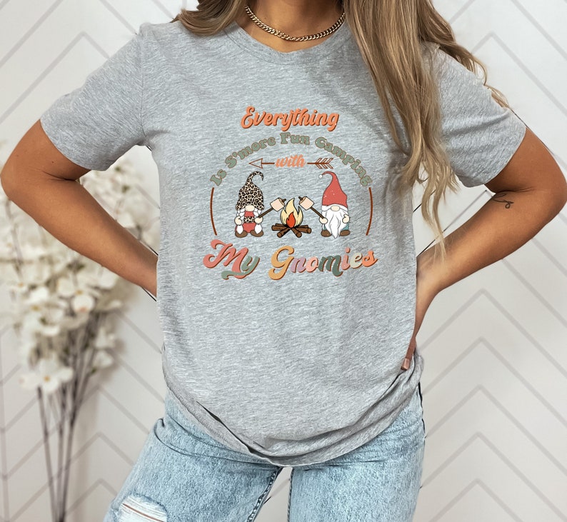 May include: A gray t-shirt with a graphic of three gnomes roasting marshmallows around a campfire. The text on the shirt reads "Everything is S'more Fun Camping with My Gnomies".