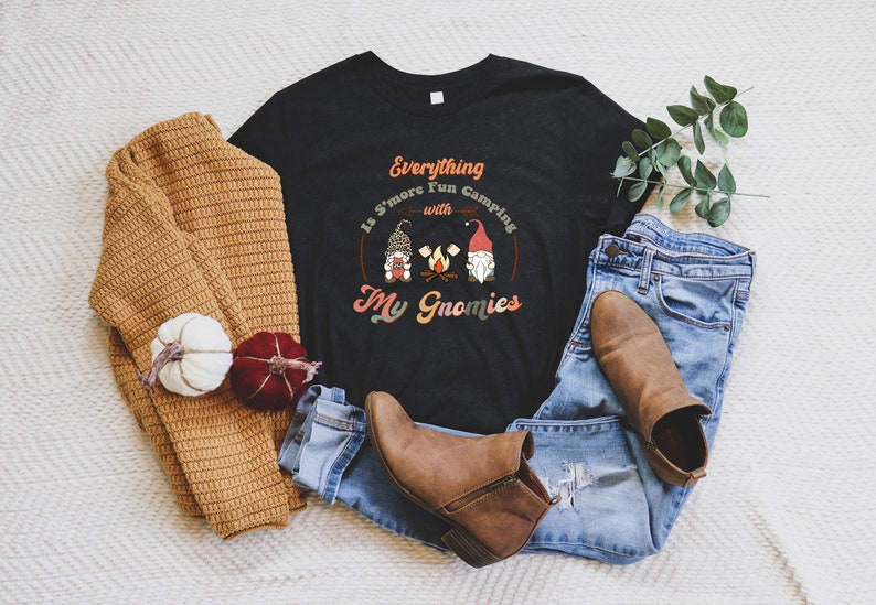 May include: Black t-shirt with a white graphic that says "Everything Is S'more Fun Camping with My Gnomies". The graphic features three gnomes around a campfire.