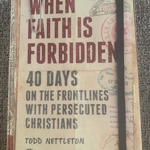 May include: A book titled "When Faith Is Forbidden: 40 Days on the Frontlines with Persecuted Christians" by Todd Nettleton. The book cover features a worn, vintage aesthetic with stamps and markings, suggesting a journey through various countries. The book is published by The Voice of the Martyrs.