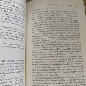 May include: Open book with a white background. The book is open to a page titled "Discipline of Perseverance" with text about the importance of perseverance in the Christian faith. The text includes quotes from the Bible and examples of how to persevere through trials and temptations.