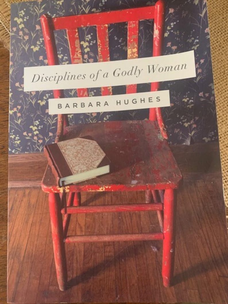 May include: A red wooden chair with a book on the seat. The chair is in front of a blue and white floral wallpaper. The book's cover is brown with gold lettering. The title of the book is "Disciplines of a Godly Woman" by Barbara Hughes.