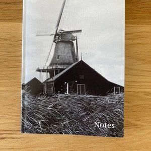 Puede incluir: Fotografía en blanco y negro de un molino de viento con un edificio negro en primer plano y hierba alta en la parte delantera. El texto "Notes" está impreso en la parte inferior de la imagen.