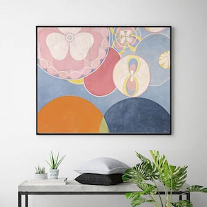 May include: Abstract art print featuring a composition of overlapping shapes in soft pastel colors. The artwork includes large pink and blue circles, an orange semi-circle, and smaller circular details, all set against a light blue background. The piece is framed in a black frame.