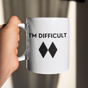 May include: White ceramic mug with black text that reads "I'm Difficult" and a black double diamond symbol.