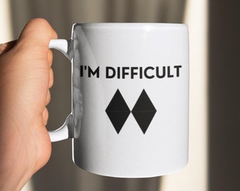 May include: White ceramic mug with black text that reads "I'm Difficult" and a black double diamond symbol.