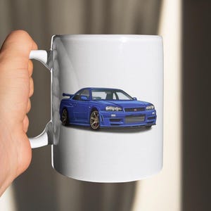 May include: A white ceramic mug featuring a blue cartoon illustration of a Nissan Skyline R34.