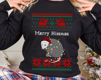 May include: Black Christmas sweater with a possum wearing a Santa hat and Christmas lights. The sweater has a red and green pattern with the text "Mexxy Hissmas".