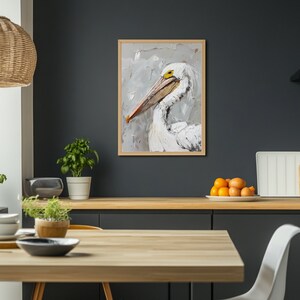Pode incluir: Uma pintura a &oacute;leo emoldurada de um pelicano branco com um bico longo e um olho amarelo, feita com pinceladas grossas e vis&iacute;veis em tons de branco, cinza e creme, sobre um fundo neutro dentro de uma moldura de madeira clara.