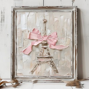 May include: A framed impasto oil painting on canvas featuring a textured Eiffel Tower in shades of beige and white, adorned with a prominent, thick-textured pastel pink bow across the center, set within a distressed white wooden frame.