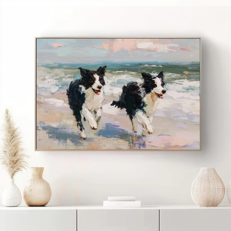 May include: A rectangular wall art print featuring an oil painting of two black and white border collie dogs running through shallow ocean waves on a sandy beach under a soft pink and blue sky, framed in a thin light wood border.