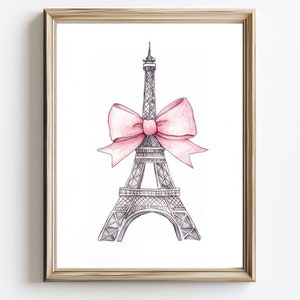 May include: A framed print featuring a watercolor illustration of the Eiffel Tower in gray, adorned with a large pink bow. The artwork is set against a white background, framed in a gold-colored frame.