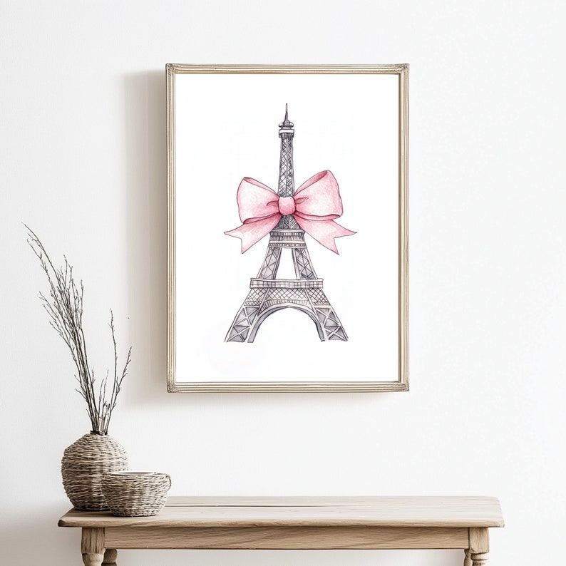 May include: A framed wall art print featuring a black and white ink-style illustration of the Eiffel Tower. A large, soft pink watercolor bow is tied around the midsection of the tower structure, creating a contrast against the white background.
