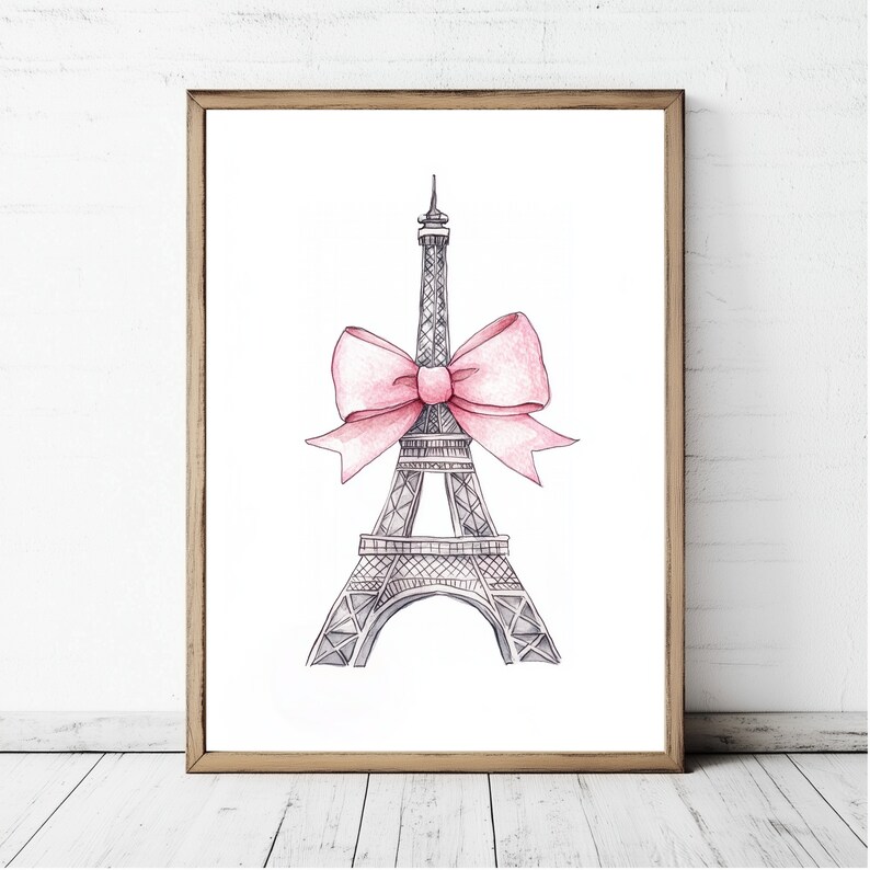 May include: A framed wall art print featuring a black and white ink-style illustration of the Eiffel Tower. A large, soft pink watercolor-style bow is tied around the middle section of the tower structure, centered against a plain white background.