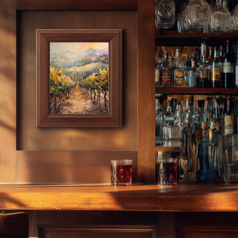 May include: A framed watercolor painting of a vineyard scene with rows of grapevines leading to distant mountains. The painting is in a dark wooden frame and hangs on a wooden wall. Two glasses of a dark liquid sit on a wooden bar.