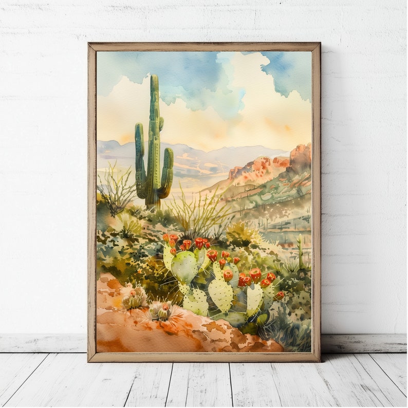 May include: Watercolor painting of a desert landscape featuring a tall saguaro cactus and prickly pear cacti with red flowers. The artwork is framed in a wooden frame and depicts a scenic view of the desert with mountains and a cloudy sky.