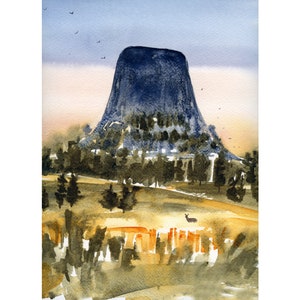 May include: Watercolour painting of Devils Tower National Monument. The artwork depicts the iconic rock formation in shades of blue and green, set against a backdrop of a soft, colourful sky. The foreground features a field with a deer.