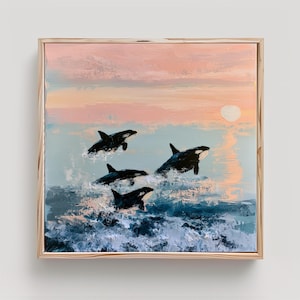 May include: A square framed oil painting depicting four black and white orcas breaching through dark blue ocean waves. The background features a soft pastel sunset with hues of pink and peach, and a pale circular sun reflecting on the water surface.