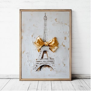 May include: Framed artwork featuring the Eiffel Tower with a gold bow. The tower is white with gold accents, set against a textured white background. The frame is a light brown color.