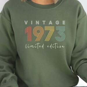 Puede incluir: Sudadera verde con el texto "Vintage 1973 edici&oacute;n limitada" en colores arco&iacute;ris.
