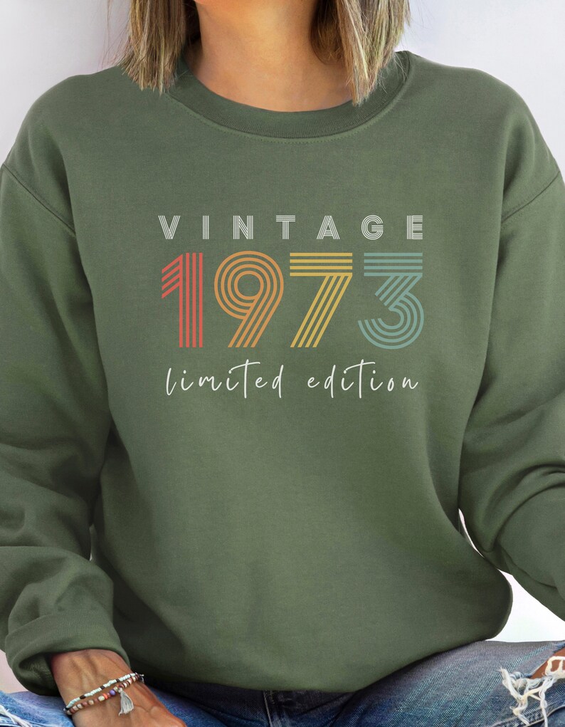 Puede incluir: Sudadera verde con el texto "Vintage 1973 edici&oacute;n limitada" en colores arco&iacute;ris.