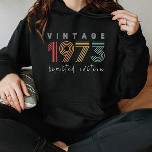 Puede incluir: Sudadera con capucha negra con el texto "Vintage 1973 edici&oacute;n limitada" en un esquema de colores arco&iacute;ris.