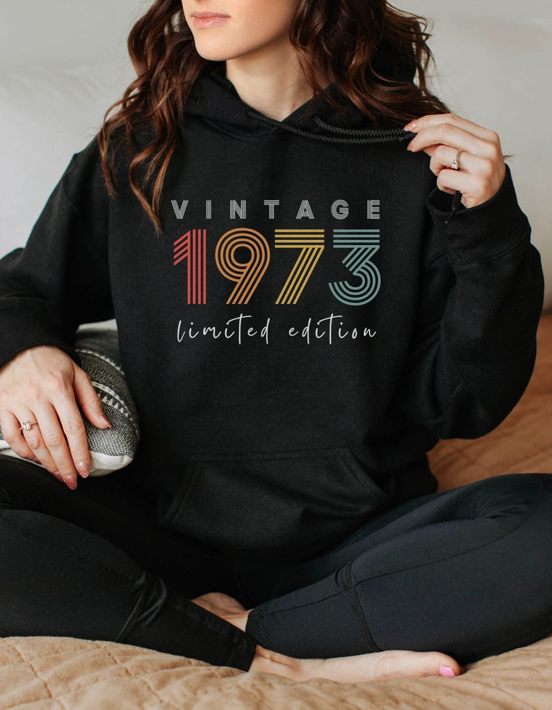 Puede incluir: Sudadera con capucha negra con el texto "Vintage 1973 edici&oacute;n limitada" en un esquema de colores arco&iacute;ris.