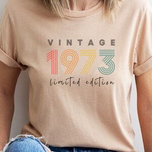 Puede incluir: Una camiseta beige con el texto "Vintage 1973 edici&oacute;n limitada" en fuente de rayas de colores.