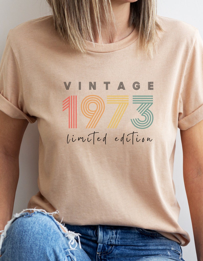 Puede incluir: Una camiseta beige con el texto "Vintage 1973 edici&oacute;n limitada" en fuente de rayas de colores.