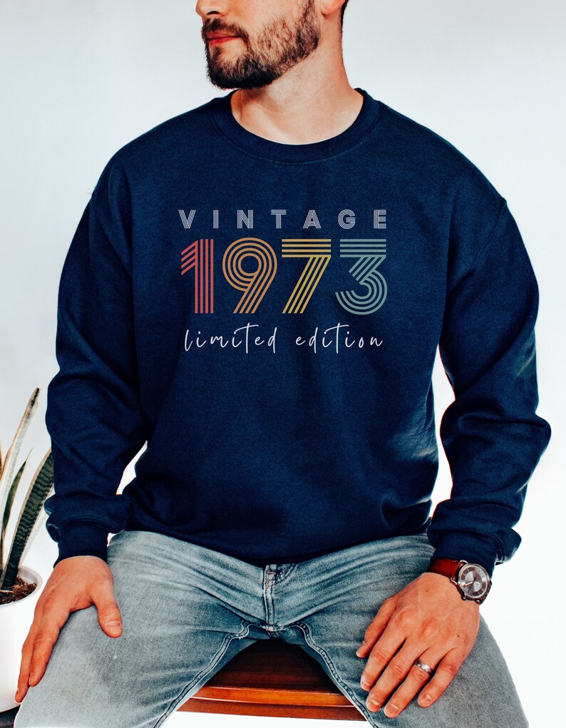 Puede incluir: Una sudadera azul marino con el texto "Vintage 1973 edici&oacute;n limitada" en un esquema de colores arco&iacute;ris.