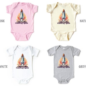 K&ouml;nnte beinhalten: Vier Baby-Bodys in verschiedenen Farben: rosa, wei&szlig;, natur und grau. Jeder Body zeigt ein Motiv eines Raumschiffs mit dem Text "I need my space".
