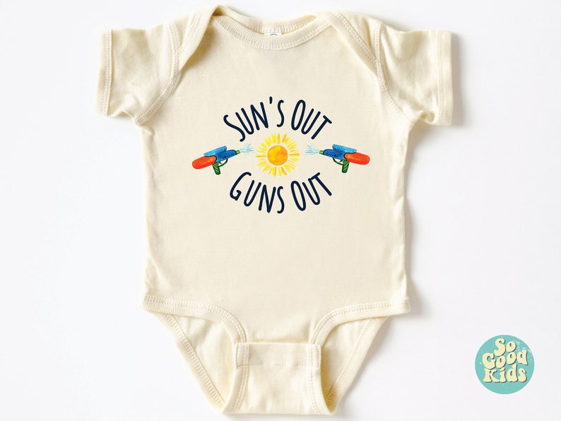 May include: Cream-colored baby onesie with the text "SUN'S OUT GUNS OUT" in navy blue. The design features a yellow sun and two water guns spraying water. A fun summer-themed outfit for babies.