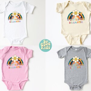 Pode incluir: Quatro bodies de beb&ecirc; em branco, bege, rosa e cinza com um gr&aacute;fico de arco-&iacute;ris e flores e o texto "A little bit dramatic".